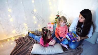 美丽<strong>的姐姐</strong>，在圣诞树和圣诞树<strong>的</strong>背景下，和坐在地毯上<strong>的小</strong>女孩玩耍